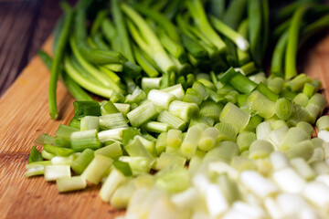 Close up of chopped fresh green spring onions stems on wooden board.