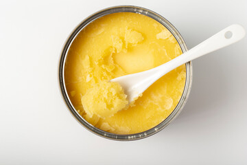 Close up of ghee butter in can with ceramic spoon on white background.