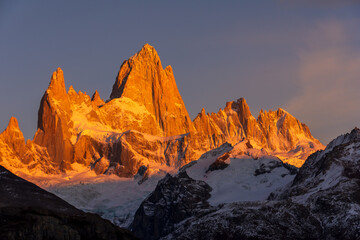 The first rays of sunlight shine on the Fitz Roy mountain, creating hues of red and orange. Fitz Roy is located near the village of El Chaltén in the Patagonia region of Argentina.