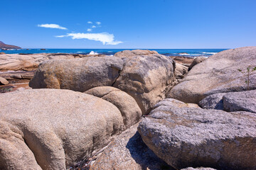 Fototapeta na wymiar Rocky coastline with the ocean and blue sky with copyspcae in the background. Stunning nature landscape or seascape of rocks. Boulders or big natural stones in the sea with beautiful rough textures