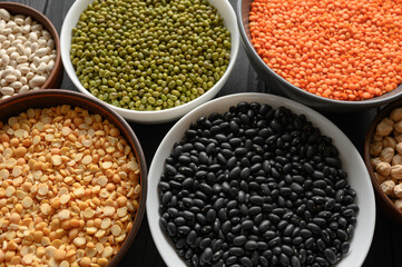 Overhead view of bowls of assorted raw legumes on a dark wooden table