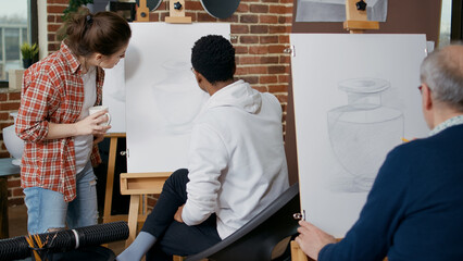 Young woman explaining artistic lesson to student in art class. Creative man using pencil and...