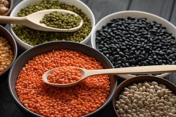 Overhead view of bowls of assorted raw legumes on a dark wooden table