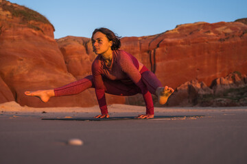 Woman doing yoga bakasana crane pose while meditating at the beach