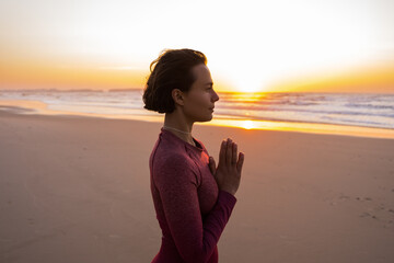 Caucasian woman standing at the beach and meditating around the wild nature during the sunset