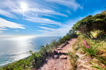Fototapeta na wymiar Copy space with scenic coast and rocky mountain slope with cloudy blue sky background. Rugged landscape of plants growing on a cliff by the sea with hiking trails to explore in Cape Town South Africa