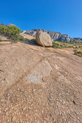 Fototapeta na wymiar Mountainside with large boulders and lush plants with copy space. Indigenous dry fynbos and wild grass growing on a rocky hill in summer warm weather. Quiet nature scene with tropical weather