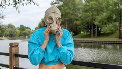 The girl puts on a gas mask on the river bank. Alienation in the city. Fashion, ecology and...