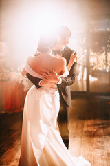 The newlyweds dance at the wedding in the warm light of the spotlight. A girl in a white wedding...