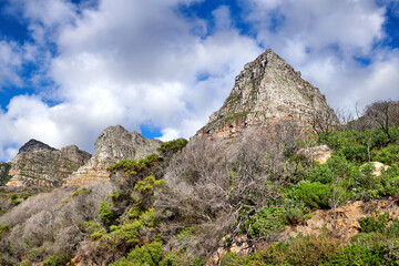 Fototapeta na wymiar Scenic landscape of mountains in Cape Town, South Africa against cloudy blue sky copy space from below. Scenic view of plants and shrubs growing on a rocky hill and cliff in a natural environment