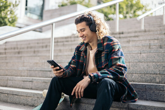 Skateboarder resting using mobile and listening to music