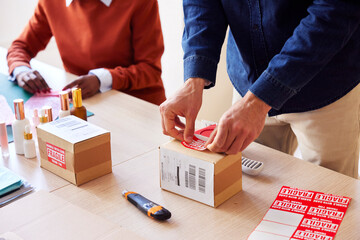 Cropped coworkers attaching fragile stickers on boxes