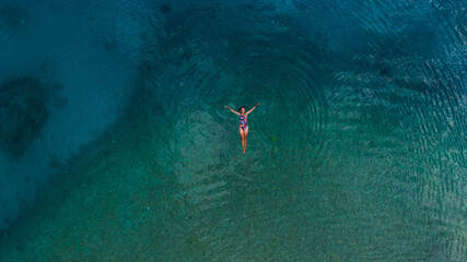 young woman in turquoise water, drone overhead