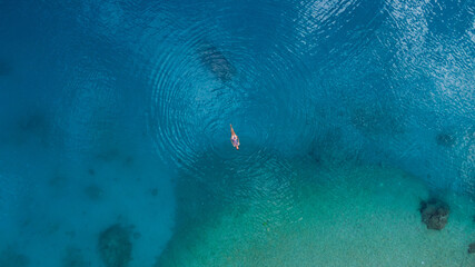 young beautiful woman laying on turquoise water, drone overhead