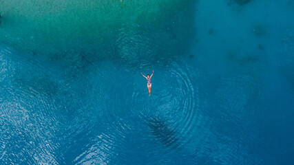 young woman floating in turquoise sea water, drone overhead