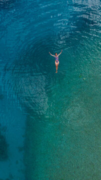 young woman relaxing in turquoise water, drone overhead