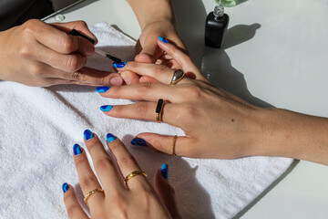 Closeup of a Woman painting blue nails on another woman 