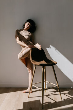 Young lady putting leg on chair and standing near wall