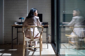 Asian manager using computer and looking out window