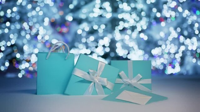 Magical forest fairy lights background. Christmas gifts in beautiful teal light blue prestige boxes with elegant white ribbons and simple satin bows on snow background. Christmas presents celebration