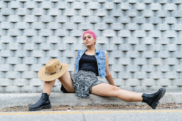 Young woman sitting on the edge of a sidewalk looking at the camera.