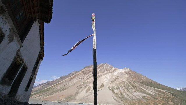 building of an ancient Buddhist monastery in the Zanskar Himalayas. Curtains and flags flutter in the wind on windows and doors, atmospheric mountain landscape around