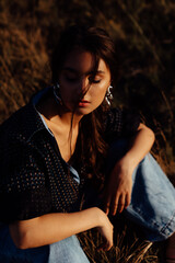 Fashionable young model in boho style clothes on a background of dry grass, field. Female beauty and style concept.