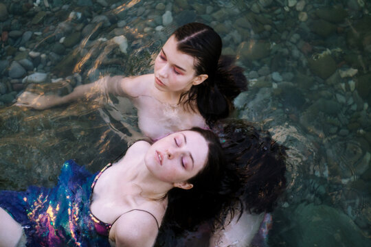 Two young women in glittering dresses swimming in sea