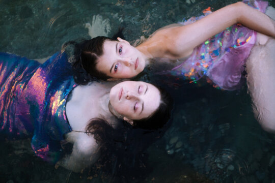 Two young women in multicolored dresses swimming in sea