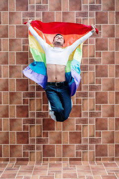 Young gay man jumping with gay flag