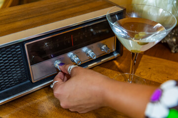 Hand turning up volume on vintage radio music with martini glass 