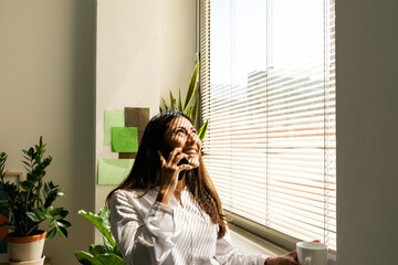 Asian woman calling by phone near the window