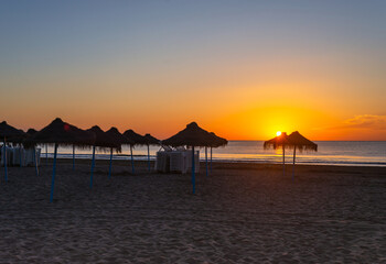 Fototapeta na wymiar scenic seascape with reed sun umbrellas at sunrise