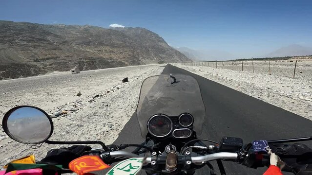 POV Motorcyclist riding motorbike by scenic mountain desert in Himalayas Tibet. Biker on motorcycle going between mountain valley by landscape path. Steering wheel view. Moto trip