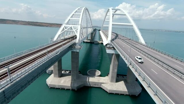 A large bridge with moving rare cars. Shot. Aerial view of a flight above bridge with turquoise water on a blue cloudy sky background.