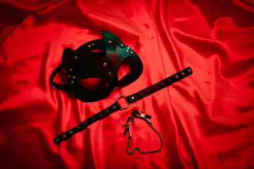 Black leather mask, necklace and nipple clamps on a red background. Love games. Love. soft focus