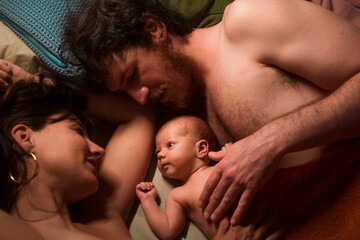 Smiling parents caressing baby on bed