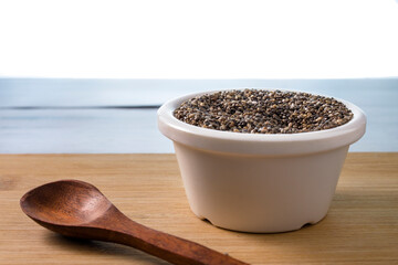 chia seeds in white ceramic bowl on white background with wooden spoon