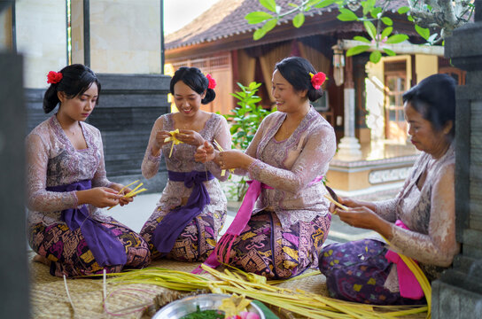 Balinese family preparing offerings together, wearing traditional 
