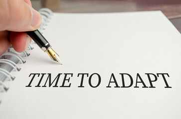 Text TIME TO ADAPT on paper notepad and pen on wooden background