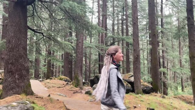young woman with long blond hair walking in forest with huge tall pine trees in Himalayas