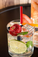 Summer refreshing mojito cocktail with strawberries, mint and lime, on dark table.