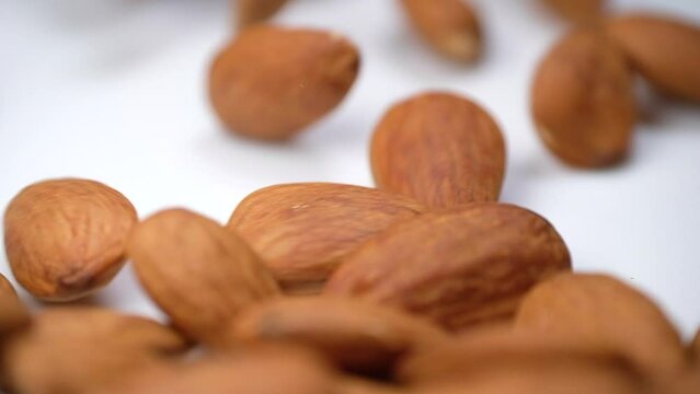 Raw almond nuts tumbling onto a white plate. An appetizing healthy vegan snack