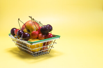 A full basket of fresh fruits bananas, cherries, nectarines, apricots, peaches on a bright yellow background is a place for text.