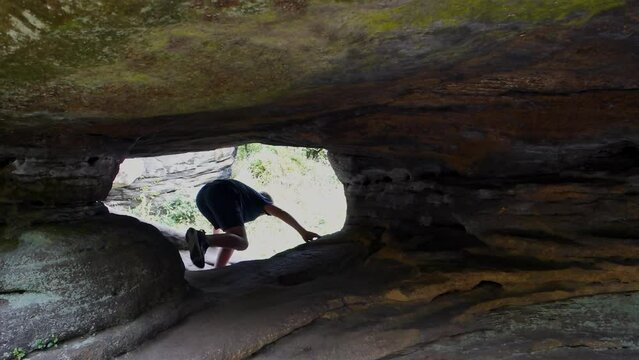 Young boy climbing and jumping on the rocks at Brimham Rocks, once known as Brimham Crags in North Yorkshire, surrounded by woodland in the UK.
