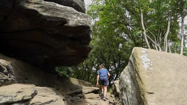 Young boy climbing and jumping on the rocks at Brimham Rocks, once known as Brimham Crags in North Yorkshire, surrounded by woodland in the UK.