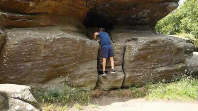 Young boy climbing and jumping on the rocks at Brimham Rocks, once known as Brimham Crags in North Yorkshire, surrounded by woodland in the UK.