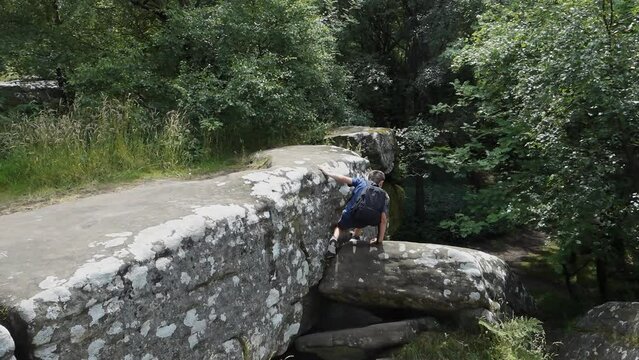 Young boy climbing and jumping on the rocks at Brimham Rocks, once known as Brimham Crags in North Yorkshire, surrounded by woodland in the UK.