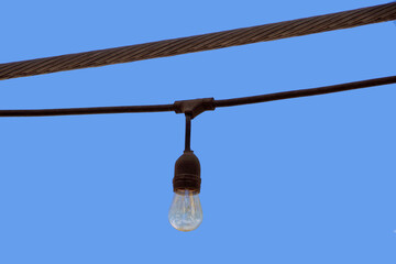 Obraz premium A single light bulb of an outdoor light chain seen against blue sky