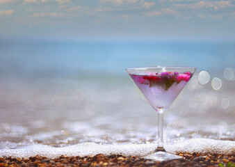 Cooling original drink with ice cubes and flowers on the beach on the sand with a sea view.
